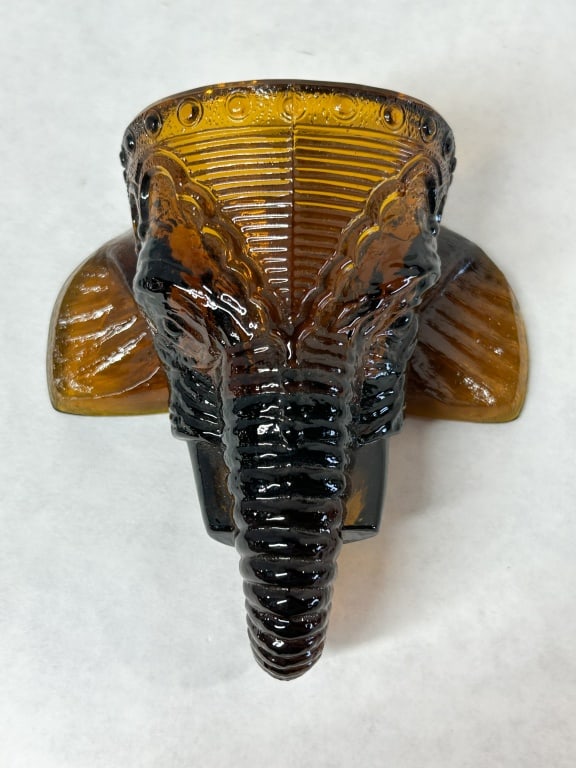 BOYD AMBER GLASS ELEPHANT WALL POCKET: A mid-century pressed glass wall pocket molded in translucent honey amber as a stylized elephant head. The high-relief decoration includes an ornate caparison, curled trunk, and outspread ears.