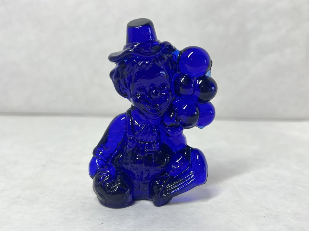 MOSSER COBALT GLASS CLOWN 1981: Mosser Glass cobalt blue figurine depicting a seated clown holding a cluster of balloons. The piece features an embossed mark reading LYLE on the rear of the overalls and a molded M 81 designation nea