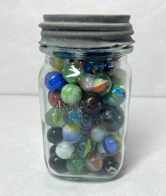 ANCHOR HOCKING VINTAGE GLASS MARBLE COLLECTION: A collection of vintage glass marbles contained in an Anchor Hocking Mason jar. The jar is embossed with the Anchor Hocking name, anchor symbol, and MASON. Several marbles within the group exhibit gre
