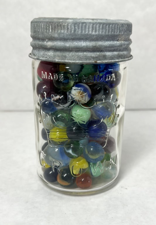 CROWN, MARBLES AND JAR, 20TH CENTURY: A Canadian glass fruit jar embossed with a stylized crown logo and text reading MADE IN CANADA and CROWN contains a collection of approximately 100+ glass marbles. The mixed assortment includes a uran