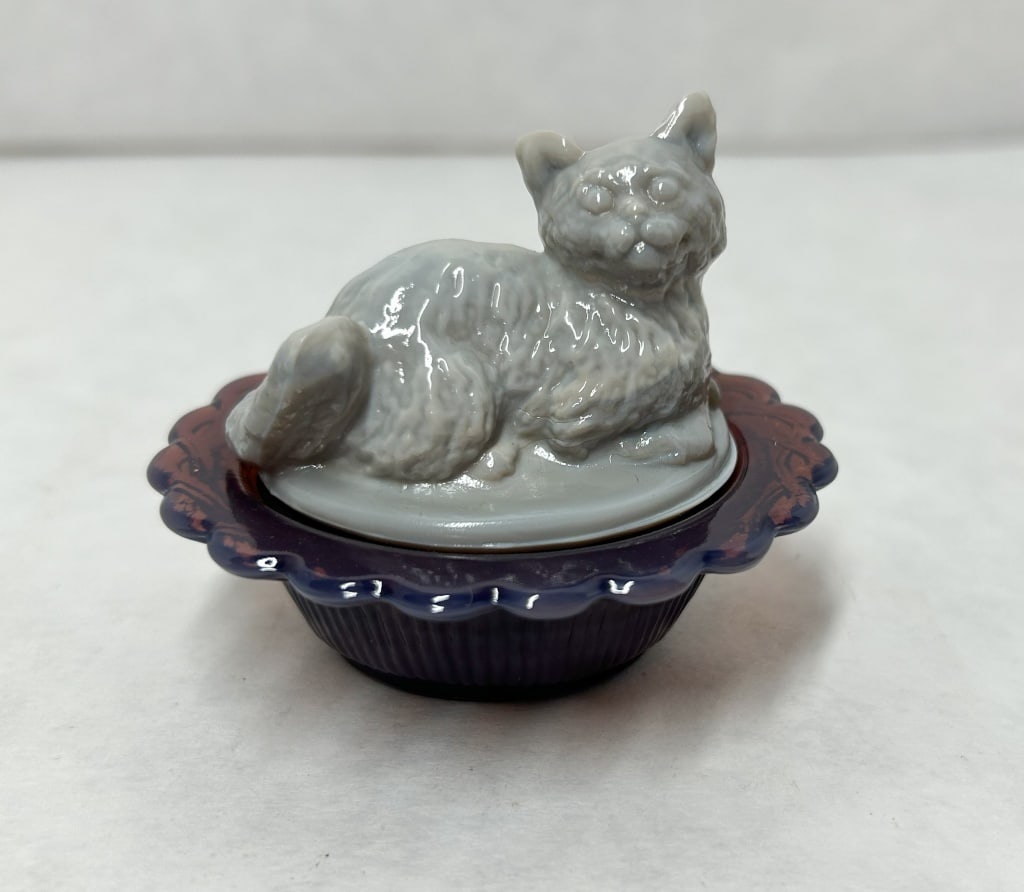 MOSSER GLASS SLAG CAT NEST: Two-piece pressed glass trinket box produced by Mosser Glass Company. A molded mark consisting of a capital M within an oval is present on the interior floor of the translucent amethyst glass base, id