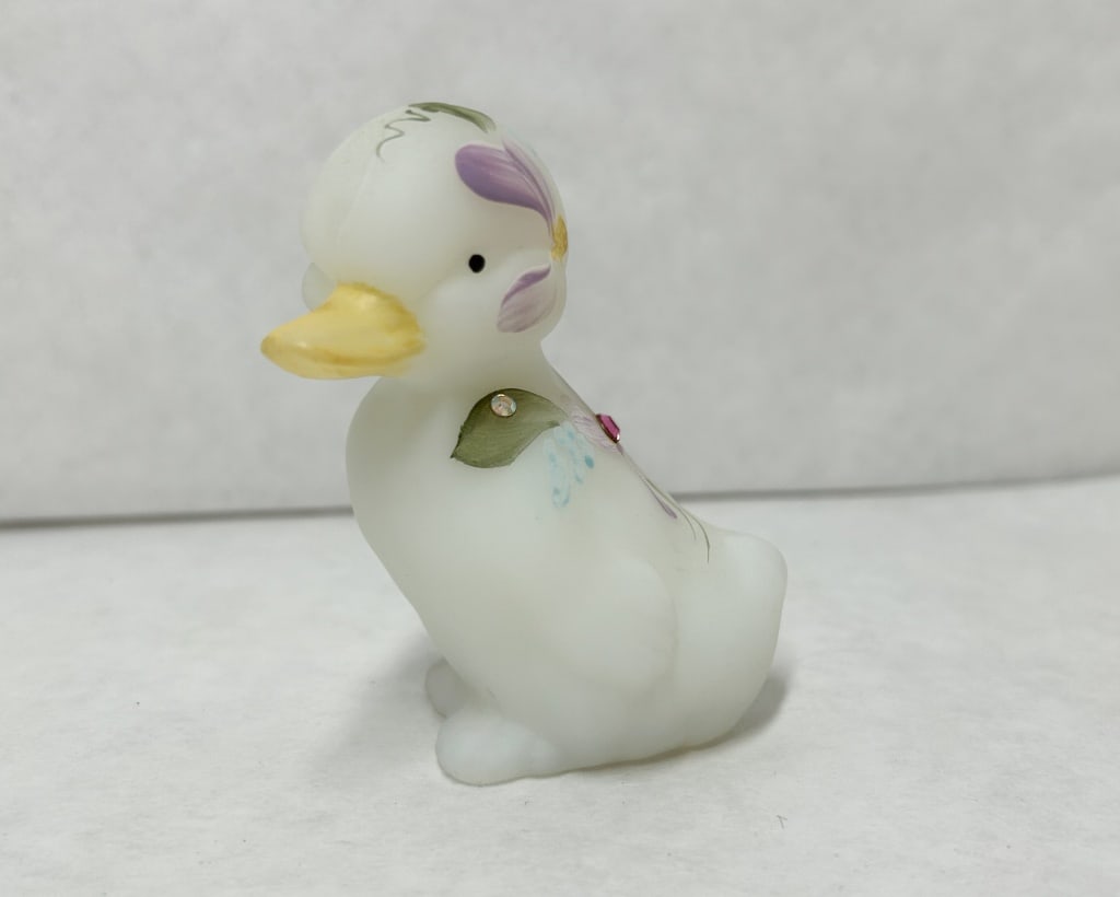 FENTON HAND PAINTED SATIN GLASS DUCKLING: A miniature satin glass duckling featuring a hand-painted lavender floral motif with light blue accents and green foliage. The decoration is embellished with two applied faceted crystals, and the base