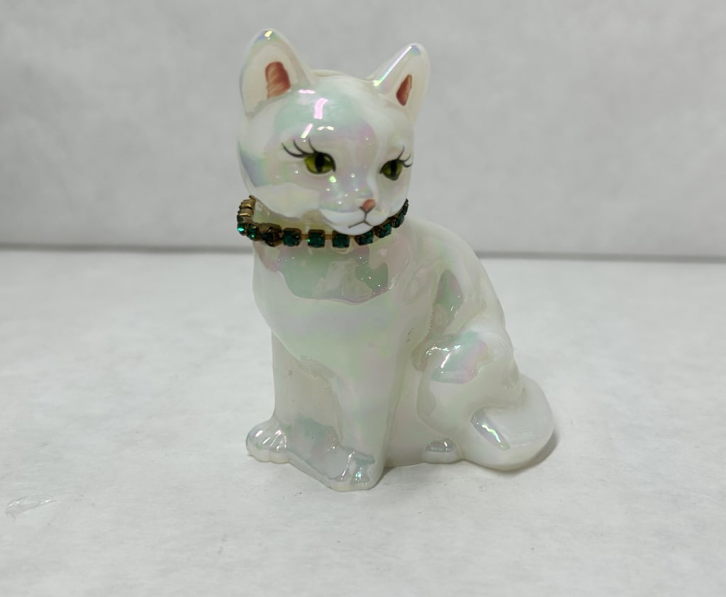 FENTON IRIDESCENT GLASS CAT FIGURINE: Fenton Art Glass seated cat figurine in white glass with an iridescent luster finish. The base features a hand-signed signature in gray ink reading S Williams, and the figure is adorned with a fixed c