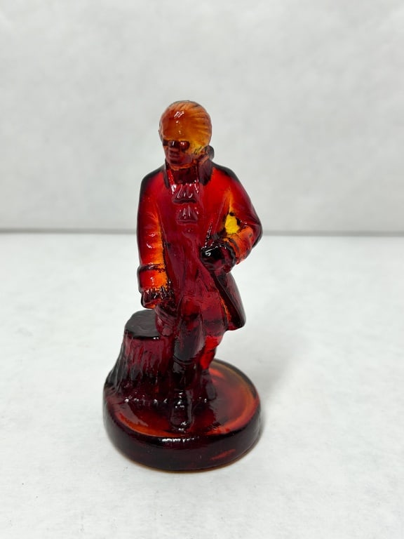 BOYD COLONIAL MAN AMBERINA GLASS FIGURINE: A pressed glass figurine of a colonial man standing beside a tree stump, executed in amberina glass. The base is embossed with an I over G monogram at the center and a B in a diamond mark on the outer