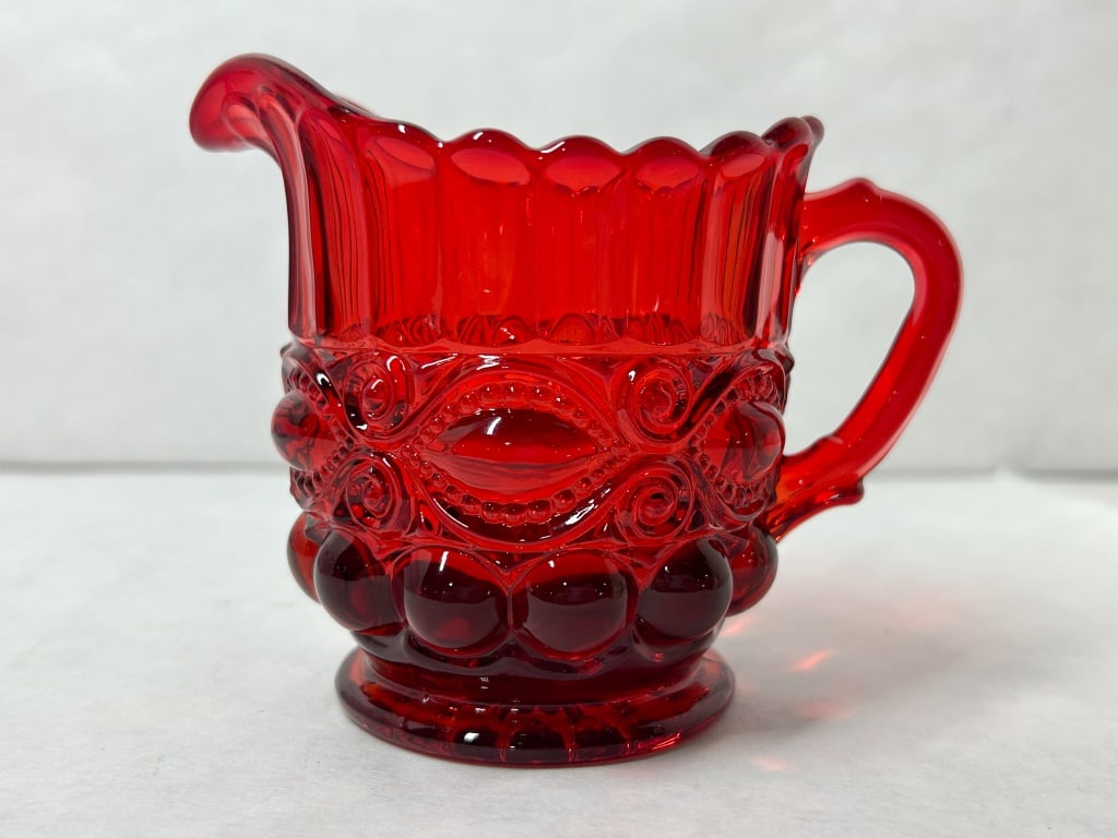 MOSSER RUBY RED EYE WINKER GLASS CREAMER: Pressed glass creamer in the Eye Winker pattern. Features a scalloped rim above a fluted neck and a body decorated with beaded scrolling motifs and circular thumbprints.