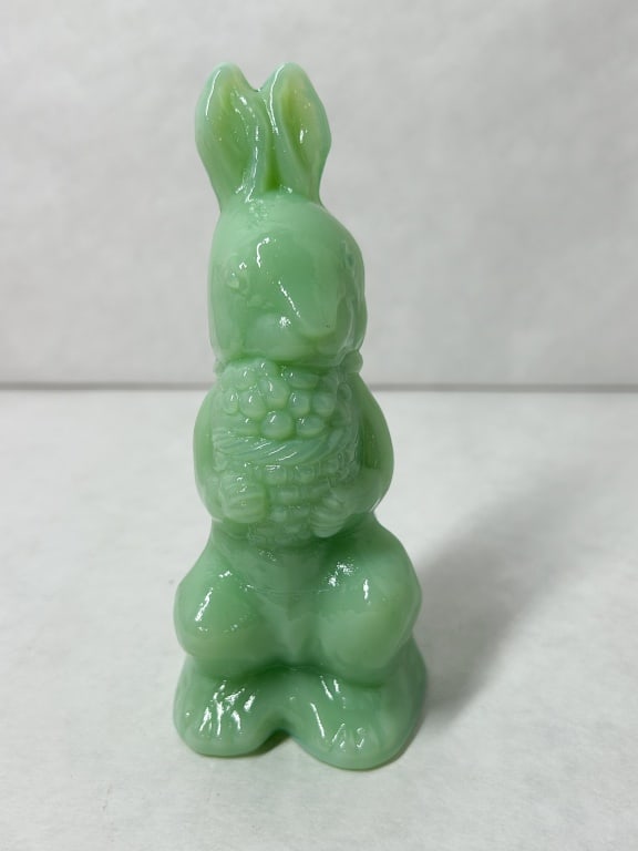 MOSSER JADEITE GLASS RABBIT WITH BASKET: A figurine of a standing rabbit holding a textured basket, produced in opaque jadeite green glass. The figure features a molded bow at the neck and a small raised mark on the lower back that is not le