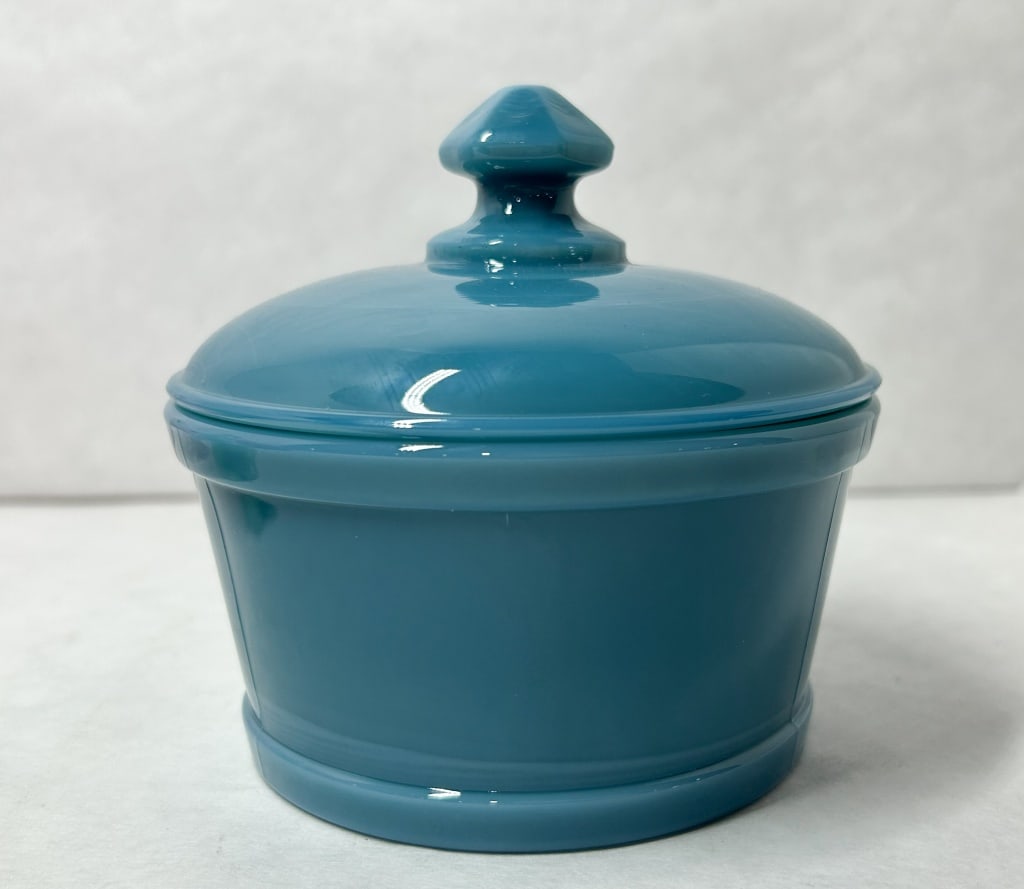 MOSSER GEORGIA BLUE GLASS BUTTER TUB: Vintage opaque turquoise blue glass lidded butter tub. The circular vessel features a tapered body with raised horizontal bands and a domed lid with a faceted pagoda-style finial.