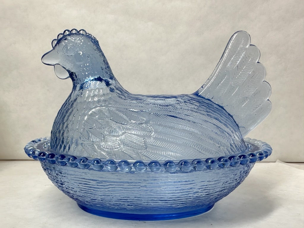 INDIANA GLASS BLUE HEN ON NEST, CIRCA 1970: A two-piece covered animal dish produced by the Indiana Glass Company in transparent light blue pressed glass, featuring a split-tail nesting hen lid and a beaded rim basketweave base. No maker marks 