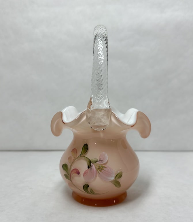 FENTON PAINTED CASED GLASS BASKET, LATE 20TH CENTURY: Fenton Art Glass hand-painted peach-colored cased glass basket featuring a white interior and an applied clear twisted handle. A silver and black foil label is affixed to the interior rim displaying a