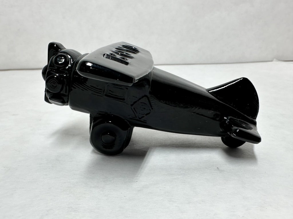 BOYD BLACK GLASS AIRPLANE, CIRCA 1980: Molded opaque black glass biplane figurine produced by Boyd's Crystal Art Glass. The upper wing features the embossed name BOYD and both sides of the fuselage bear an impressed mark consisting of a B 