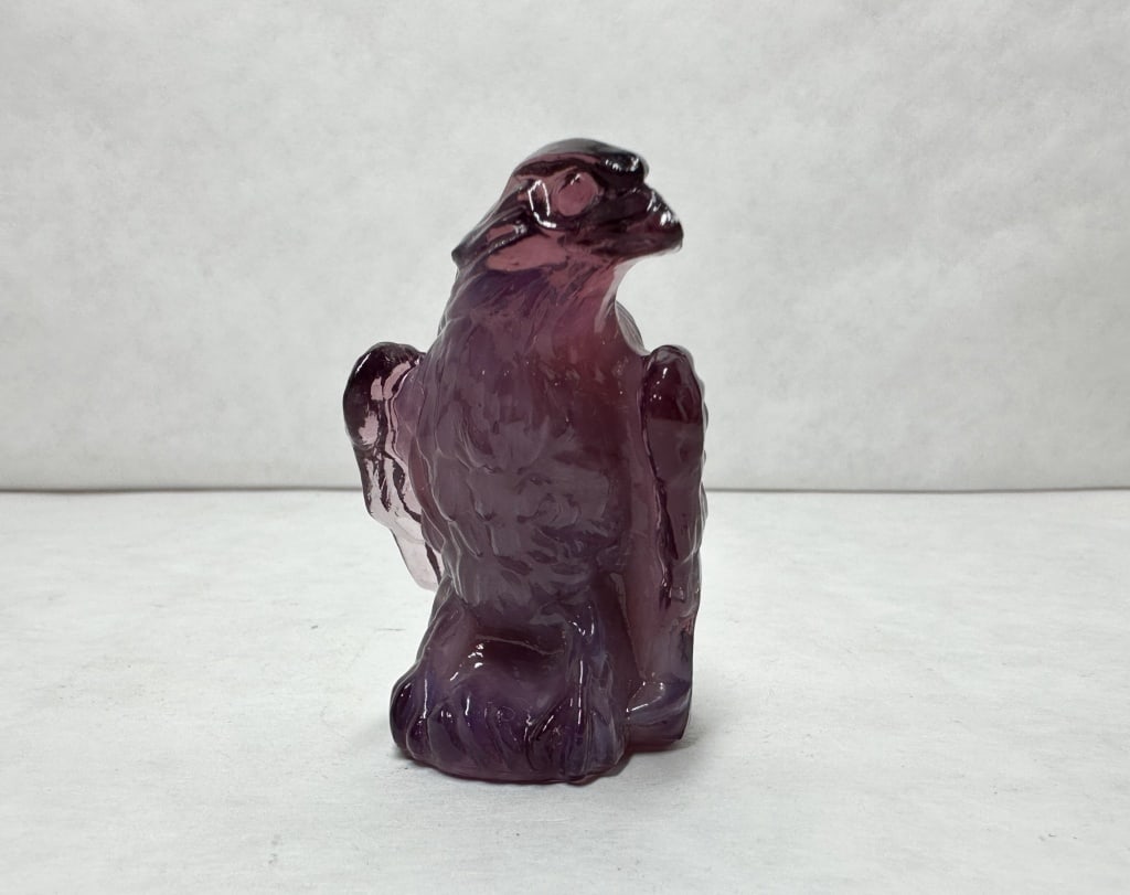 BOYD BERNIE EAGLE AMETHYST GLASS: A molded glass eagle figurine in translucent amethyst purple. The subject is depicted perched on a rock-form base with textured feathering.