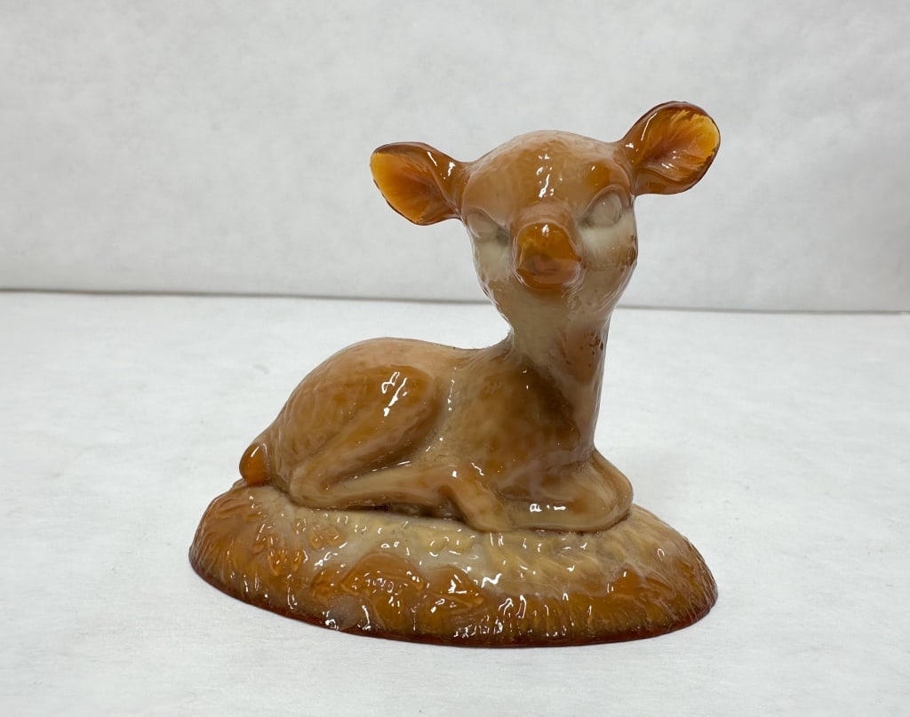 BOYD BINGO DEER CARAMEL SLAG GLASS: A caramel slag glass figurine depicting a recumbent fawn resting on a textured oval base. The opaque glass is characterized by marbleized swirls of amber-brown and cream tones with a fire-polished