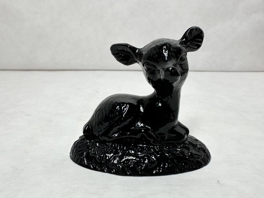 BOYD BINGO DEER BLACK GLAZED: A ceramic figurine of a reclining fawn finished in a uniform, high-gloss black glaze. The figure is modeled in an alert resting pose upon a mounded base with a molded grass texture.