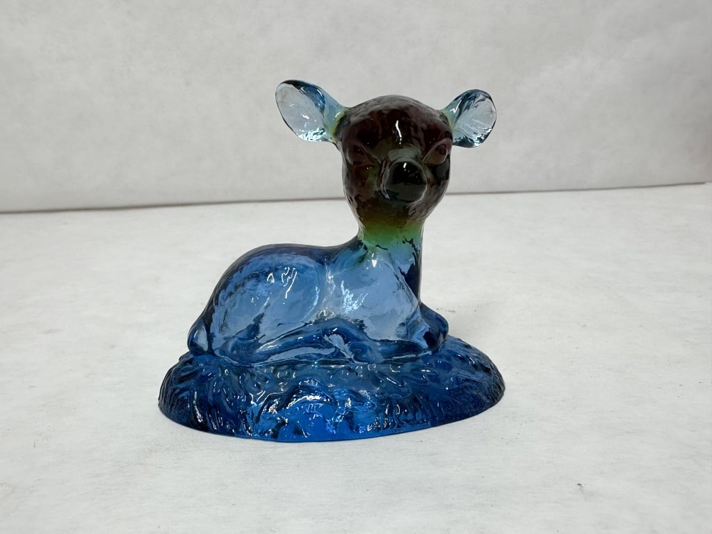 BOYD BINGO DEER BLUE RAINBOW: Art glass figurine depicting a reclining fawn with a sommerso-style color transition from amber to green and blue. The figure is set upon a textured oval base designed to resemble grass.