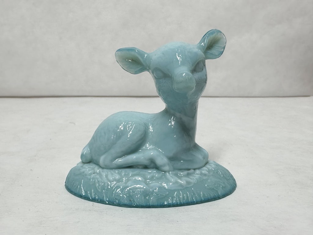 BOYD BINGO DEER BLUE SLAG GLASS: A pressed slag glass figurine depicting a reclining fawn in swirled blue and white tones. The figure is modeled in a resting pose atop an oval base with a textured grassy motif.
