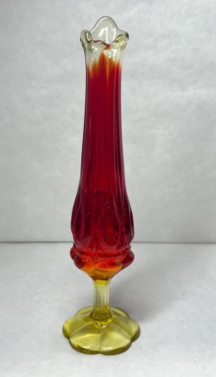 AMBERINA SWUNG GLASS VASE, 1960S: Amberina swung glass bud vase featuring a six-lobed petal foot and thumbprint pattern base. The lower section exhibits a bright yellow-orange fluorescence under ultraviolet light due to cadmium conten