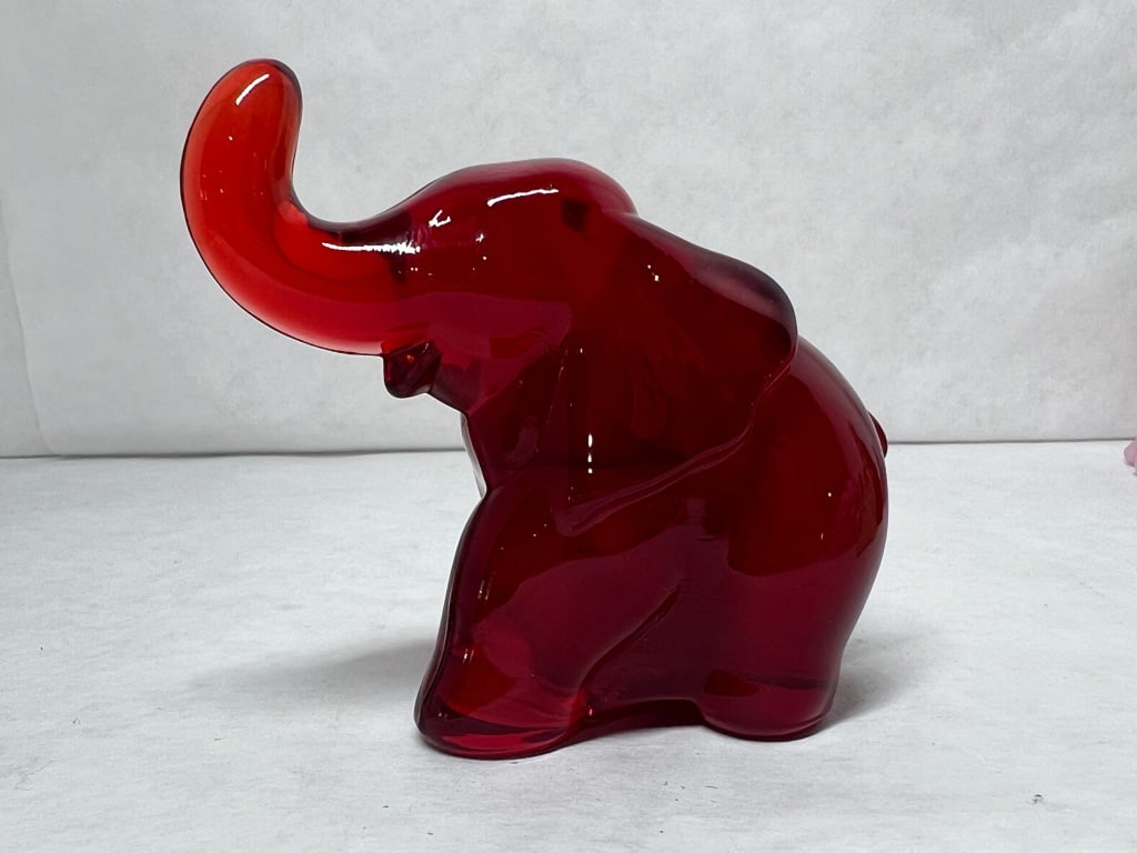 RUBY RED GLASS ELEPHANT, 20TH CENTURY: A stylized elephant figurine crafted from translucent ruby red pressed glass. The figure is depicted with an upturned trunk and features a visible vertical mold seam from production.