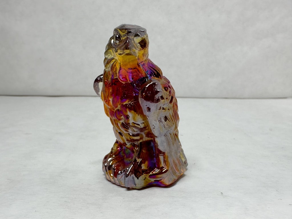 BOYD BERNIE EAGLE IRIDIZED CARNIVAL GLASS FIGURINE: A pressed glass figurine depicting a perched hawk or eagle on a textured rocky outcrop. The piece is finished with a heavy iridescent luster over an amber ground, exhibiting a range of violet, blue, a