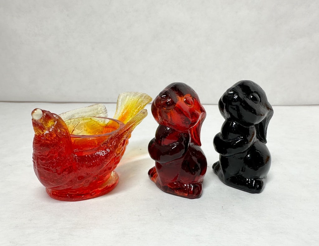 BOYD AMBERINA AND BLACK GLASS FIGURINES, LATE 20TH CENTURY: A trio of American pressed glass animal figures comprising a bird-form open dish and two standing rabbit figurines. The rabbits feature an embossed capital letter B inside a diamond cartouche on the l