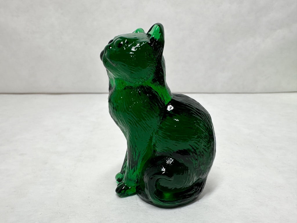 MOSSER SITTING CAT EMERALD GREEN: A seated cat figurine looking upward, crafted from translucent emerald green pressed glass. The piece features molded fur texture throughout the body and shows no visible maker marks or signatures.