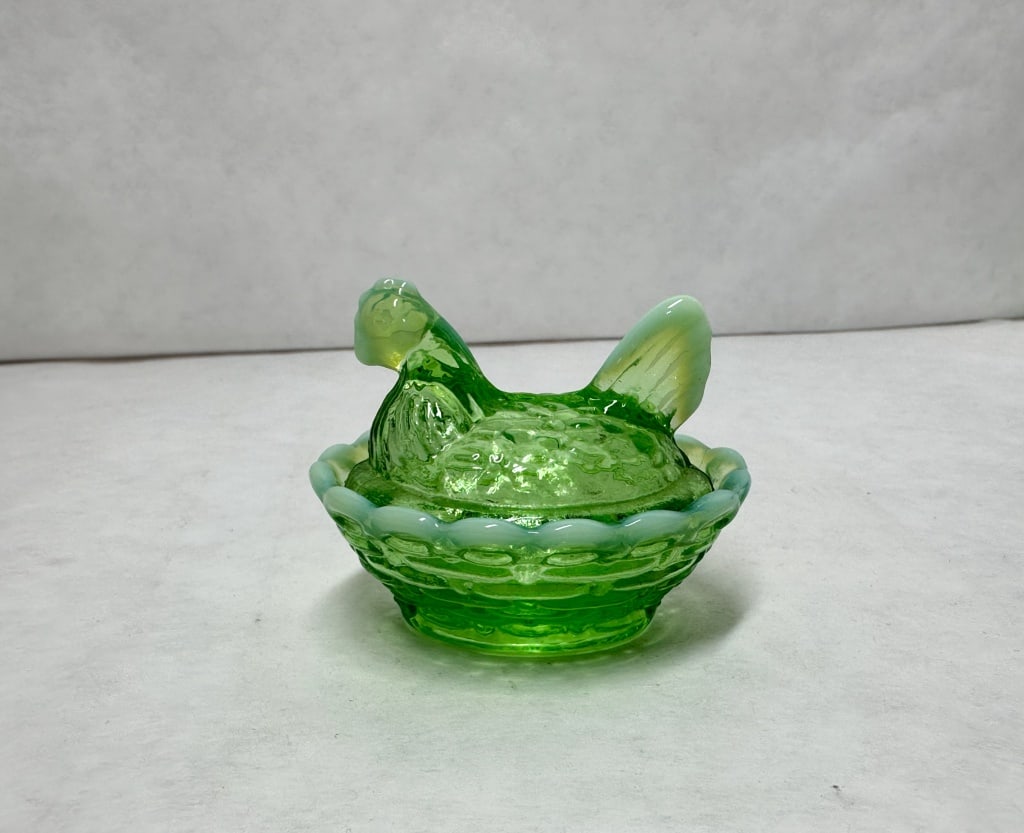 BOYD MINI GREEN OPALESCENT GLASS HEN ON NEST: A miniature pressed lime green glass covered dish featuring white opalescent highlights to the extremities and rim. The two-piece vessel is modeled as a textured hen seated upon a basketweave base.