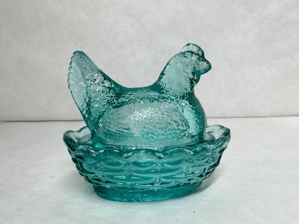MOSSER TEAL HEN ON NEST: A two-piece teal pressed glass covered dish featuring a nesting hen with a stippled feather texture and a basketweave base with a scalloped rim. The glass exhibits a strong pinkish-orange fluorescence