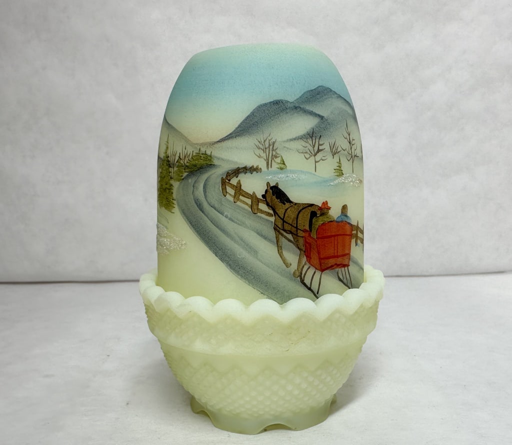 FENTON CUSTARD GLASS FAIRY LAMP, 1980: A two-piece fairy lamp constructed of uranium-bearing custard glass featuring a hand-painted winter landscape. The dome-shaped shade is painted with the year 1980 and displays a bright green fluoresce