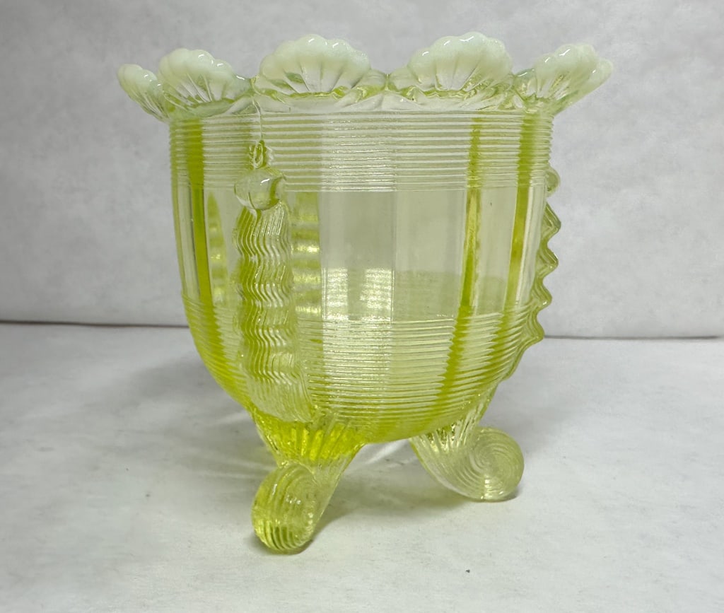CANARY OPALESCENT URANIUM GLASS BOWL, CIRCA 1900: A Victorian-era pressed uranium glass footed bowl featuring a canary opalescent finish and crimped side fins. The vessel stands on three scroll feet and exhibits a strong green fluorescence under ultr