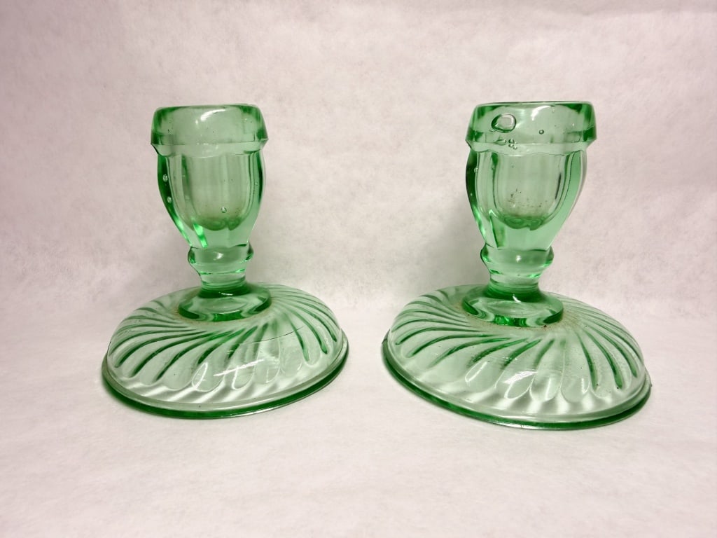 PAIR OF GREEN URANIUM GLASS SWIRL CANDLESTICKS: A pair of light green Depression-era glass candlesticks featuring a molded swirl optic pattern on the domed bases. The paneled stems and flared sockets are composed of transparent glass that exhibits 