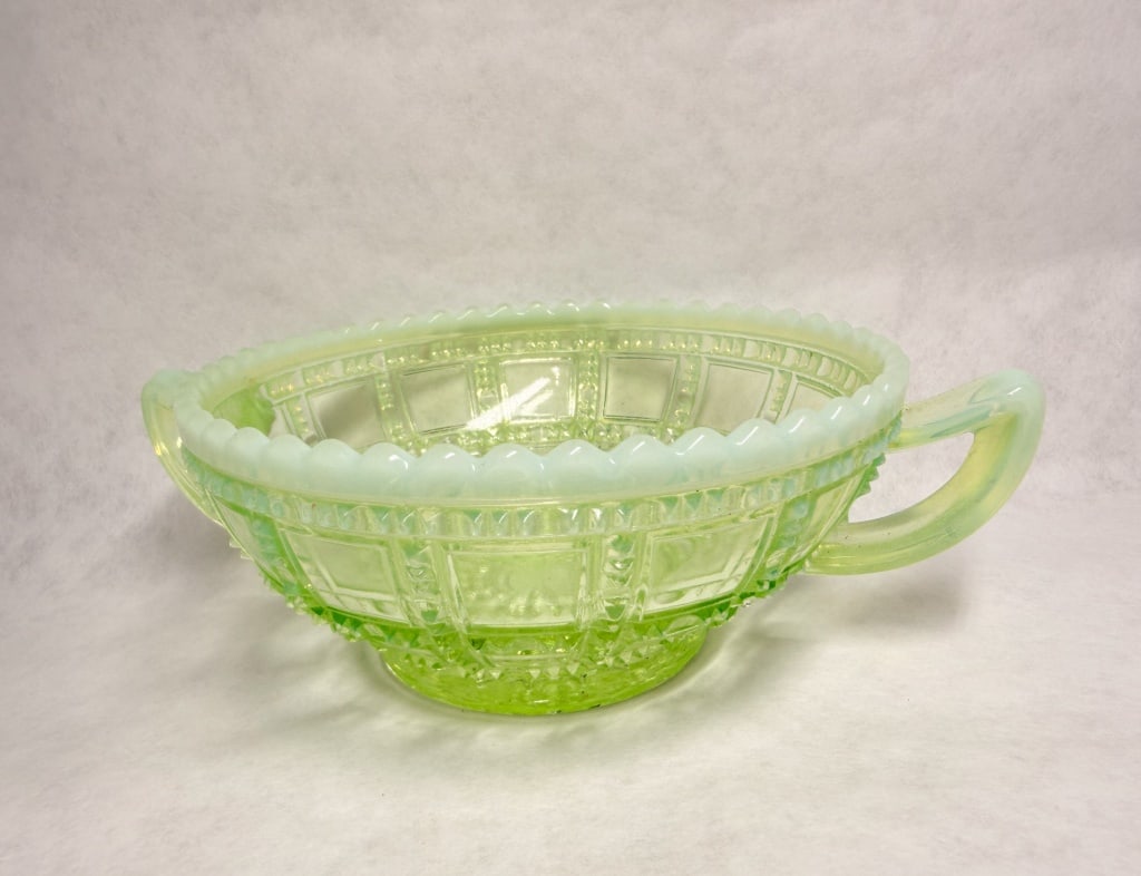BEADED BLOCK URANIUM OPALESCENT GLASS DISH, CIRCA 1905: Pressed glass two-handled bon-bon dish in the Beaded Block pattern. The piece is crafted of translucent yellow-green uranium glass with a milky white opalescent rim and handles. No maker marks are vis