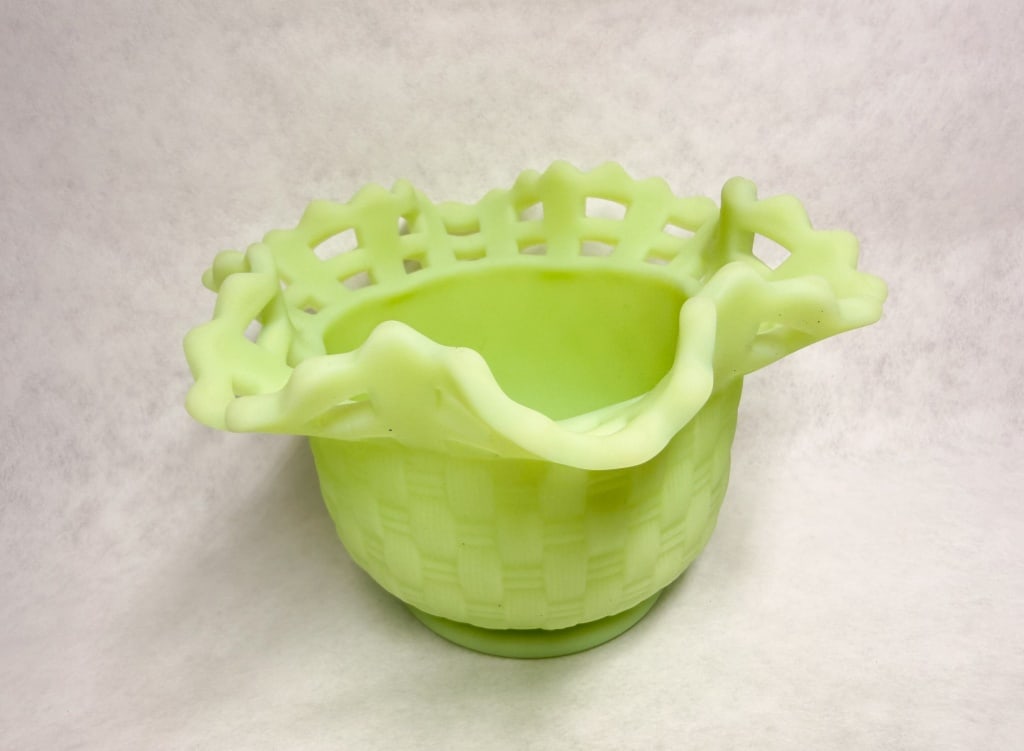URANIUM CUSTARD GLASS BASKETWEAVE BOWL, 1950s: Pressed uranium custard glass bowl featuring a basketweave body and hand-fashioned ruffled open-edge lattice rim. The piece displays a brilliant green fluorescence under ultraviolet light and bears no