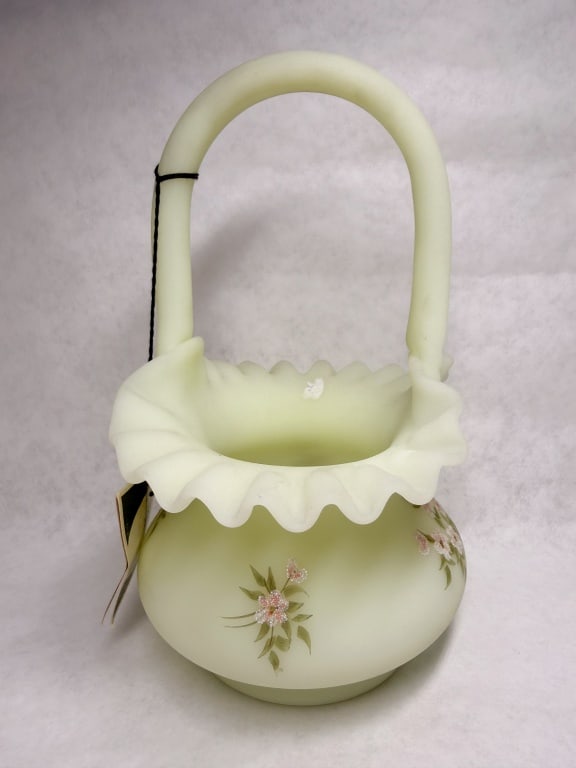 FENTON CUSTARD URANIUM GLASS BASKET: Hand-painted custard satin glass basket produced by Fenton Art Glass Company featuring a ruffled rim and applied handle. The piece bears a hand-painted signature reading Hand Painted by Lisa W. on the