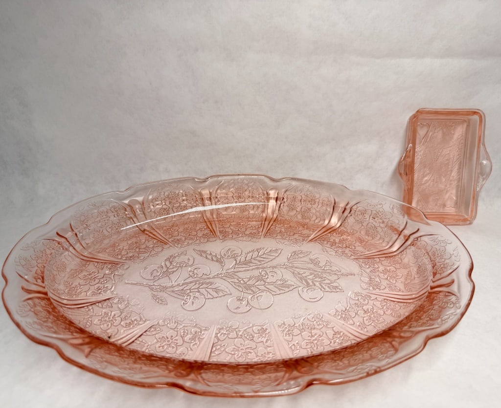 JEANNETTE TWO PINK GLASS PIECES, 1930S: Two pink Depression glass pieces produced by the Jeannette Glass Company, comprising a Cherry Blossom pattern oval platter and a Queen of Hearts playing card tray. The platter features a central cherr