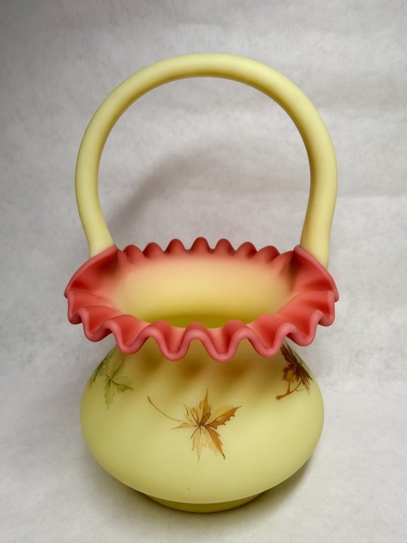 FENTON BURMESE SATIN GLASS BASKET: Hand-painted Burmese satin glass basket produced by Fenton Art Glass Company featuring an autumnal maple leaf motif. A black and gold foil label and a molded script F in an oval mark are located on th