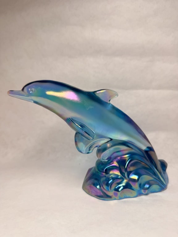 FENTON IRIDESCENT GLASS DOLPHIN, 1970S: A Fenton Art Glass Company figurine depicting a leaping dolphin upon a cresting wave. The translucent blue glass is finished with a pearlescent iridescence, and the underside features an incised oval 