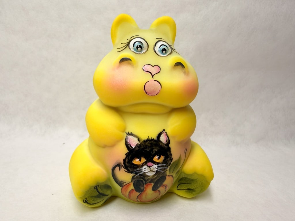 MICHELLE KIBBE HAND-PAINTED CUSTARD HIPPO, 2021 53/55: Hand-painted by artist Michelle Kibbe on a satin custard glass hippo blank, the piece features a whimsical Halloween motif of a black cat seated upon a pumpkin. The base bears a hand-painted signature