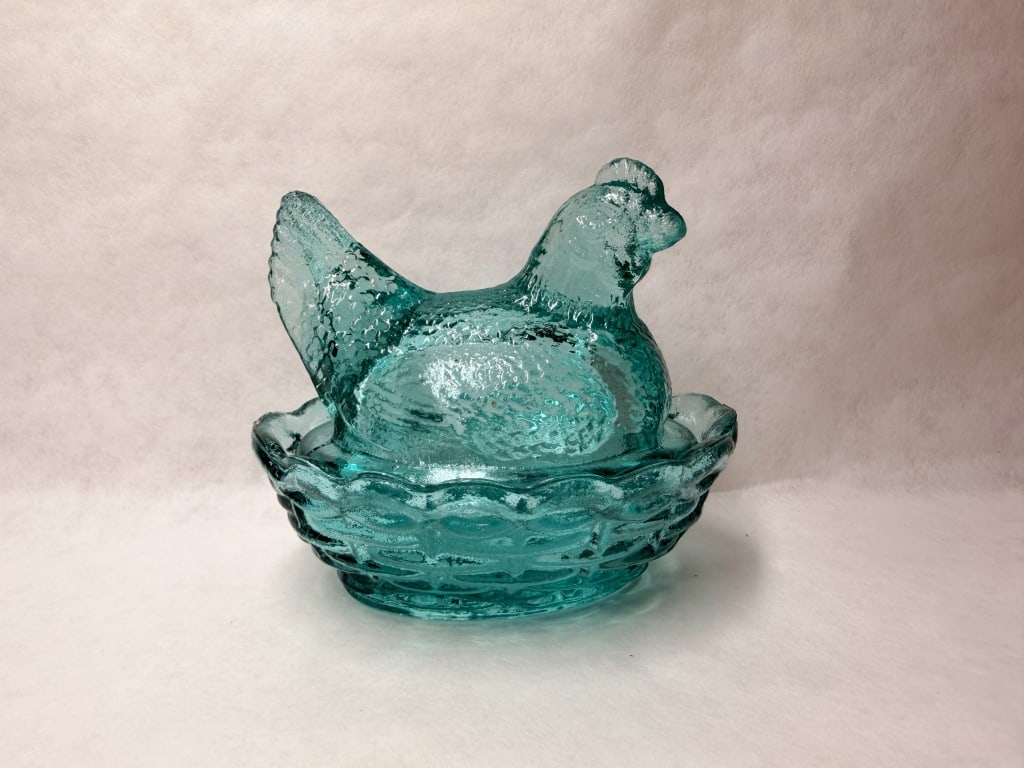 MOSSER AQUA GLASS HEN ON NEST: A vintage two-piece pressed glass covered dish featuring a turquoise blue hen lid atop a basketweave base. The glass displays a strong pinkish-orange fluorescence under ultraviolet light