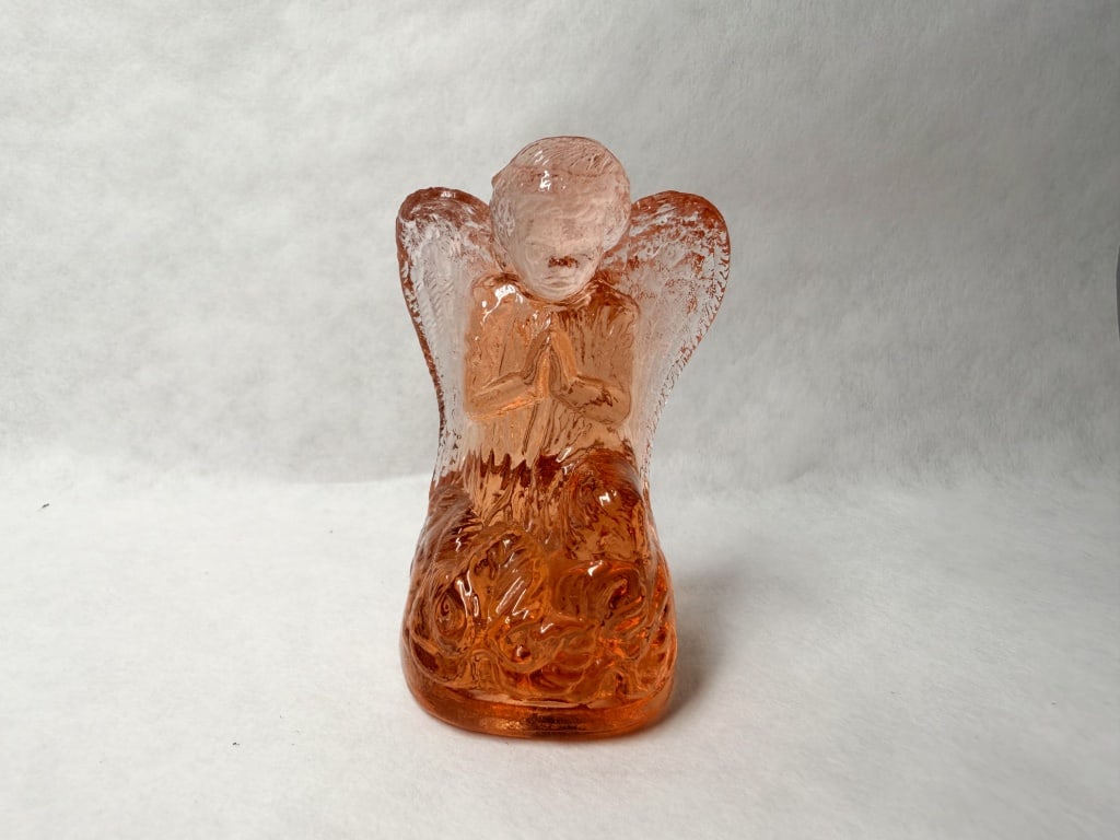BOYD PEACH URANIUM ANGEL 1970: peach-colored glass figurine of a kneeling angel. The manufacturer is identified by a monogram known to consist of an I within a G, here visible as a raised mark within a circular recessed area on the