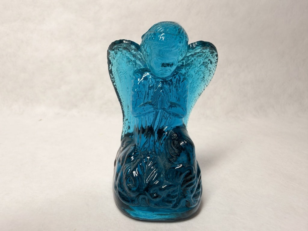 BOYD BLUE GLASS PRAYING ANGEL, LATE 20TH CENTURY: A translucent blue pressed glass figurine depicting a kneeling angel in prayer. An impressed circular mark is located on the center of the base, containing a single character that is not legible as a 
