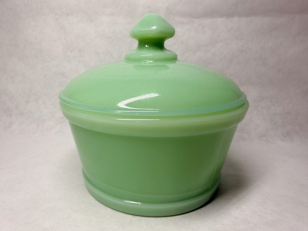 MOSSER JADEITE GLASS BUTTER TUB: A vintage lidded butter tub composed of opaque light green jadeite glass. The vessel features a stepped circular base and a matching domed lid with a faceted finial, bearing no visible maker marks on 