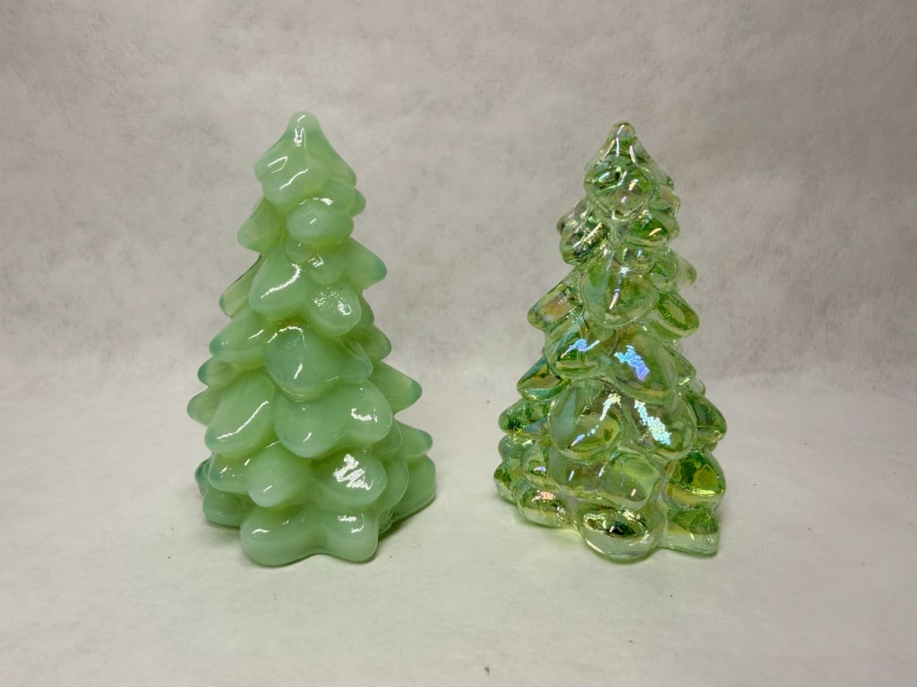 MOSSER MINI JADEITE GREEN CHRISTMAS TREES: A pair of decorative glass Christmas tree figurines featuring a tiered bough design. The set includes one opaque jadeite and one translucent green figurine, each exhibiting an iridescent aurora