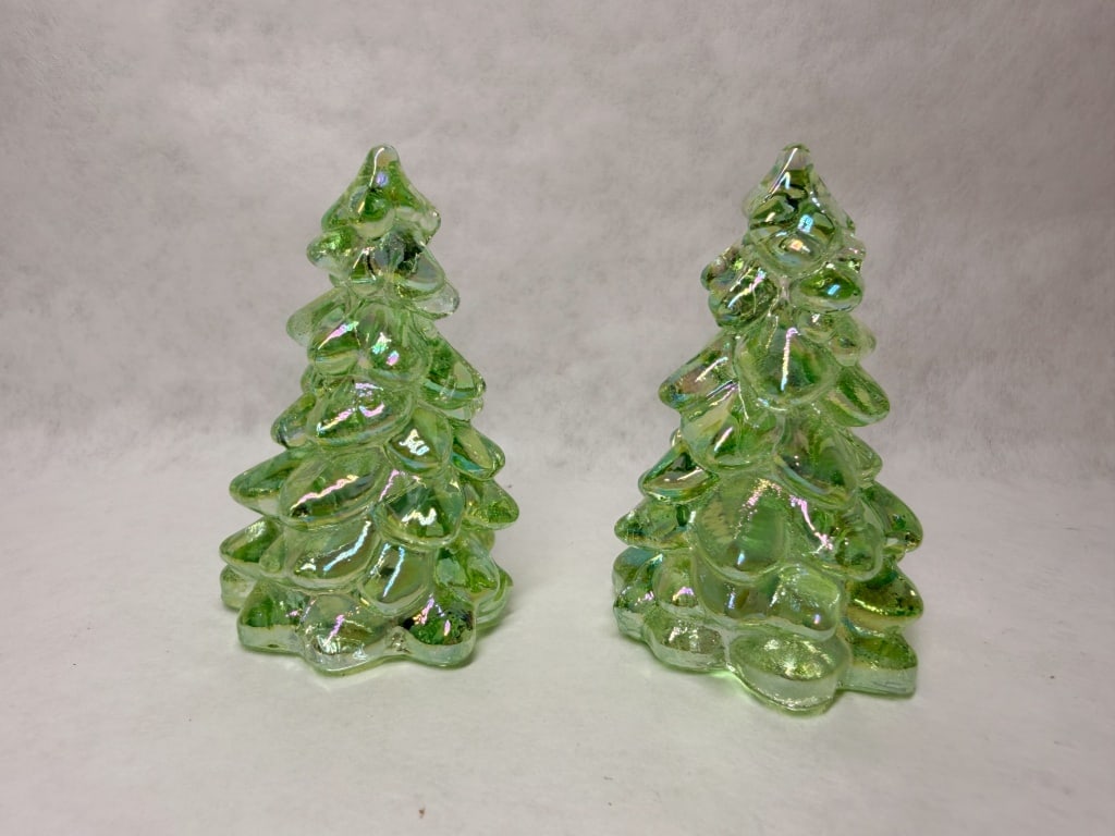 MOSSER MINI PAIR OF IRIDESCENT GREEN GLASS TREES: A pair of molded evergreen tree figurines crafted in translucent green glass with a multi-colored iridescent luster finish. The stylized trees feature a tiered branch design and exhibit a shimmering