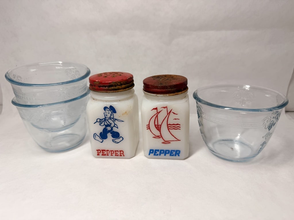 HAZEL-ATLAS BLUE AND MILK GLASS, C. 1940: A collection of Hazel-Atlas Glass Company sapphire blue bowls in the Royal Lace pattern and white milk glass pepper shakers. The shakers feature transfer-printed graphics of a Dutch boy and
