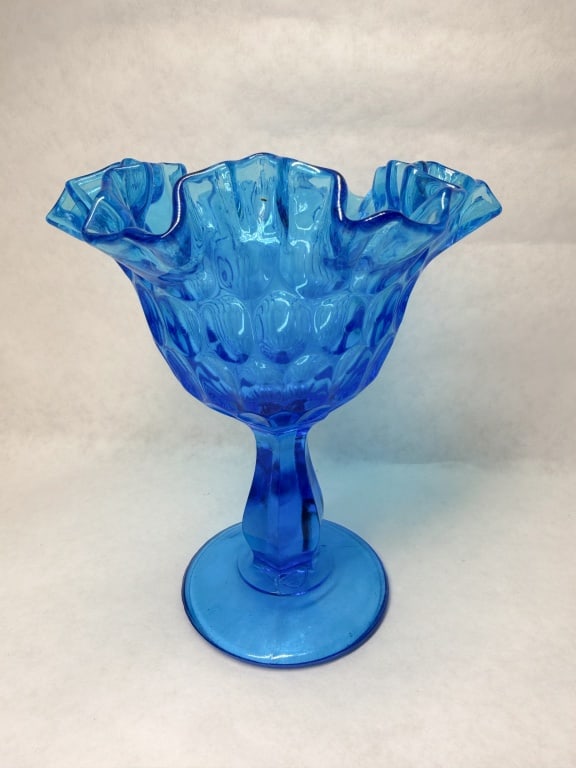 FENTON COLONIAL BLUE GLASS COMPOTE CIRCA 1970: A Fenton Colonial Blue art glass compote featuring a thumbprint optic pattern and a deeply ruffled rim. The bowl is supported by a hexagonal stem on a circular foot which bears an embossed script