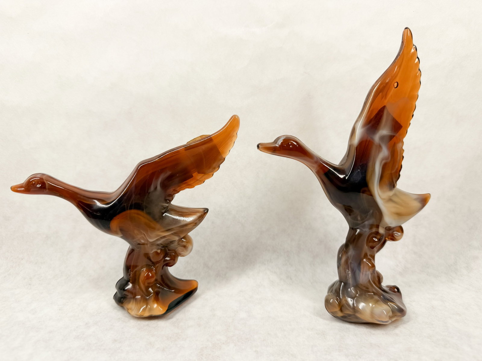 IMPERIAL CARAMEL SLAG MALLARDS, 1970S: A pair of mallard duck figurines produced by the Imperial Glass Company in marbled caramel slag glass. The pieces retain original square orange foil labels reading CARAMEL SLAG END O'DAY GLASS by