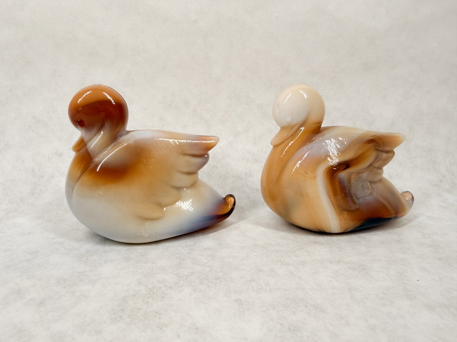 IMPERIAL CARAMEL SLAG WATERFOWL: Caramel slag glass waterfowl figurines, one depicting a duck and the other a cygnet. The molded forms feature white and tan marbleized swirls with blue highlights; no maker marks are visible on the un