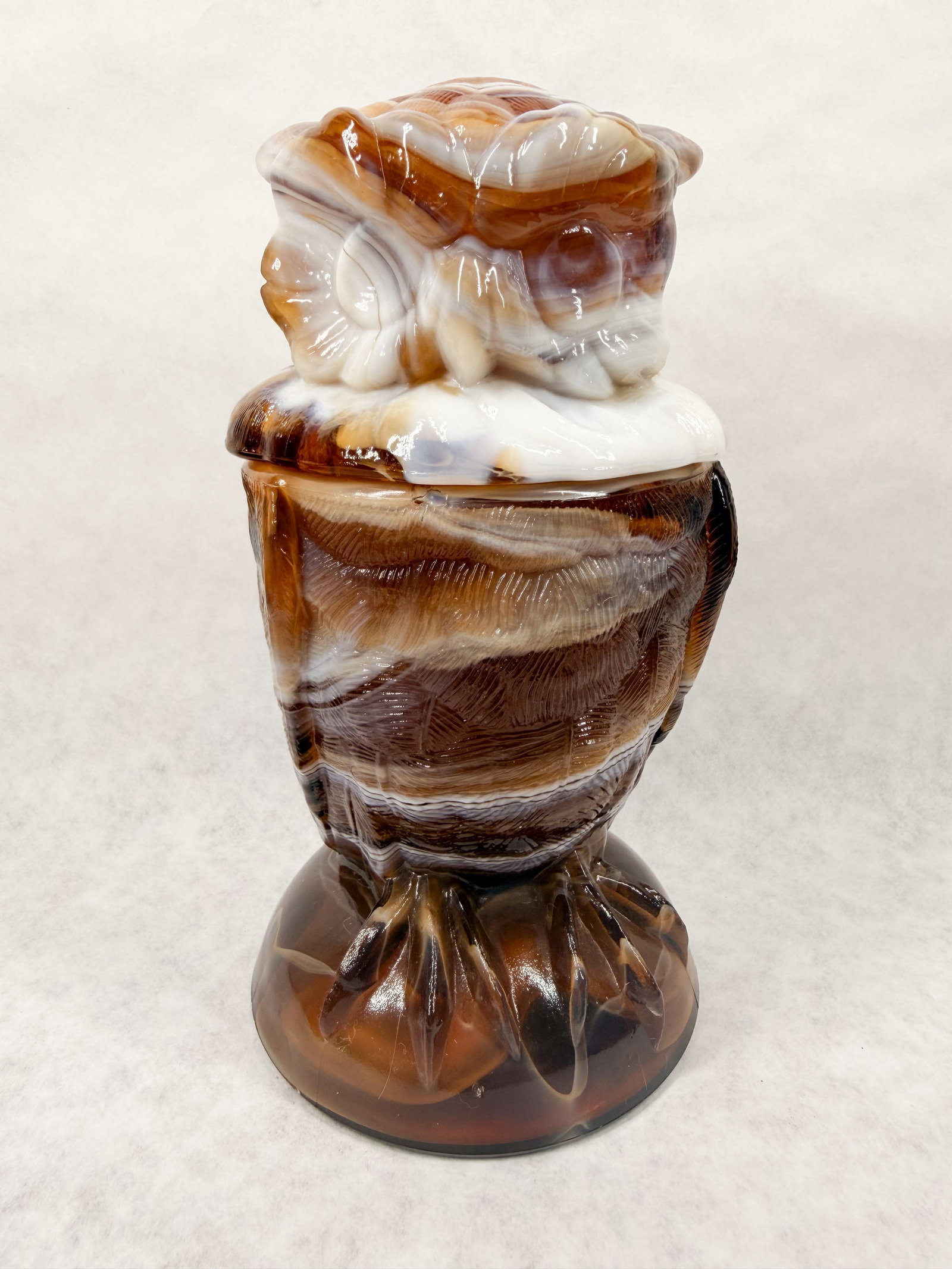 IMPERIAL CARAMEL SLAG GLASS OWL JAR: Lidded figural jar in the form of an owl, crafted from molded caramel and white slag glass. The body and lid feature textural feather details and stylized facial features, with an illegible raised mar
