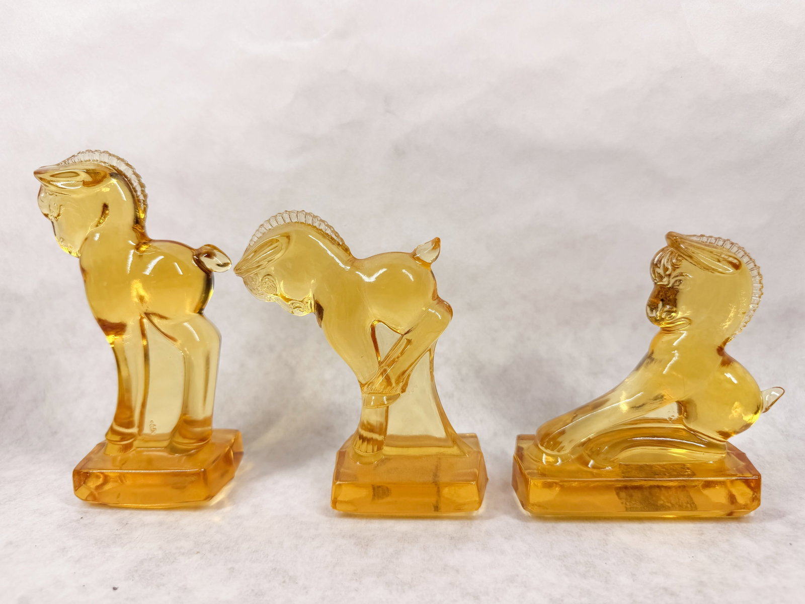 HEISEY BY IMPERIAL AMBER GLASS FOAL TRIO: A trio of stylized pressed amber glass horse figurines produced by Imperial Glass Company. Each piece bears an embossed mark of a large capital letter G containing a smaller vertical capital letter I,