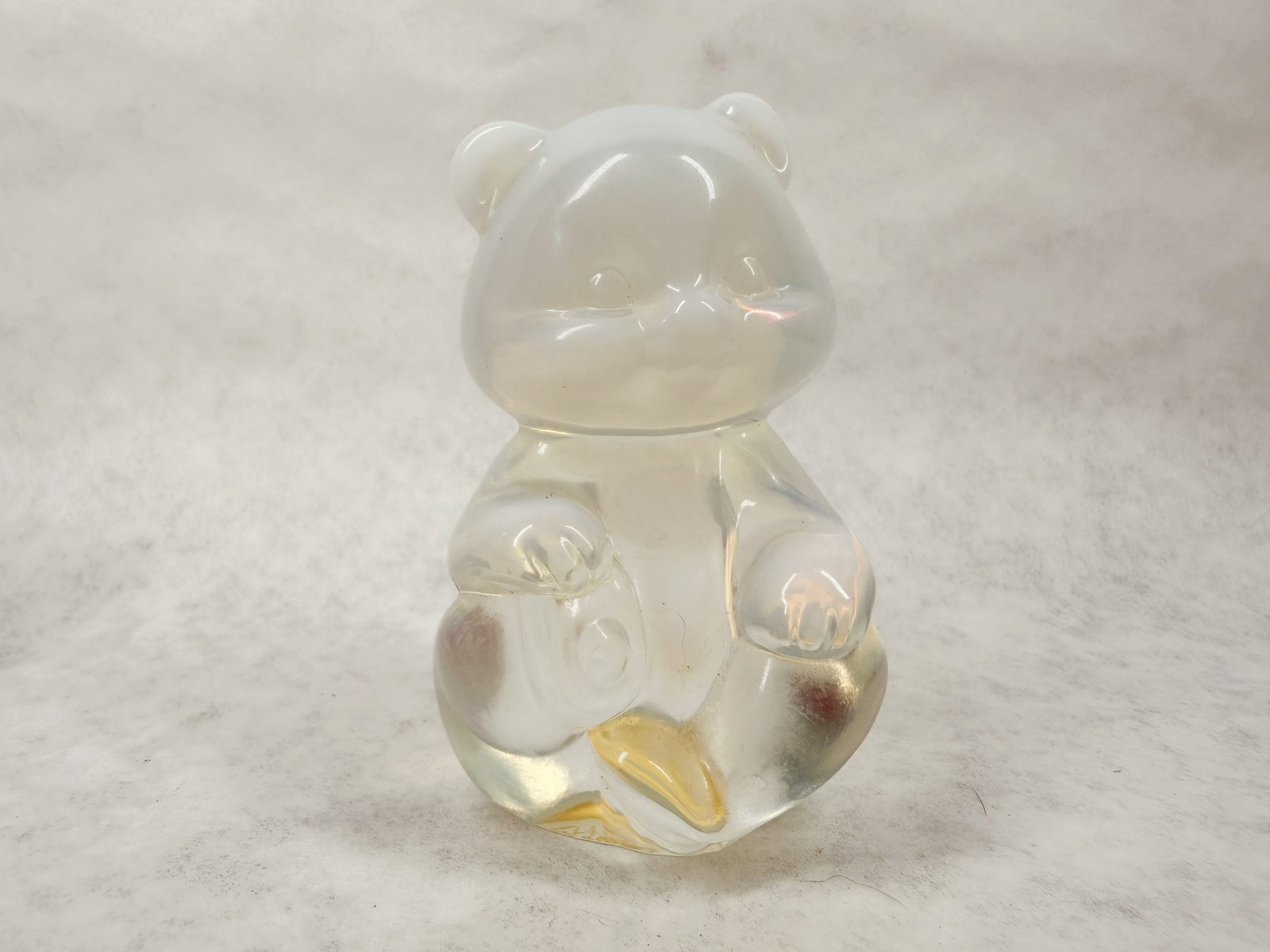 FENTON OPALESCENT GLASS BEAR, 1995: Seated glass bear figurine produced by Fenton Art Glass. An oval gold foil label with Fenton in script and a partially torn white label reading 90th Anniversary are present on the base.