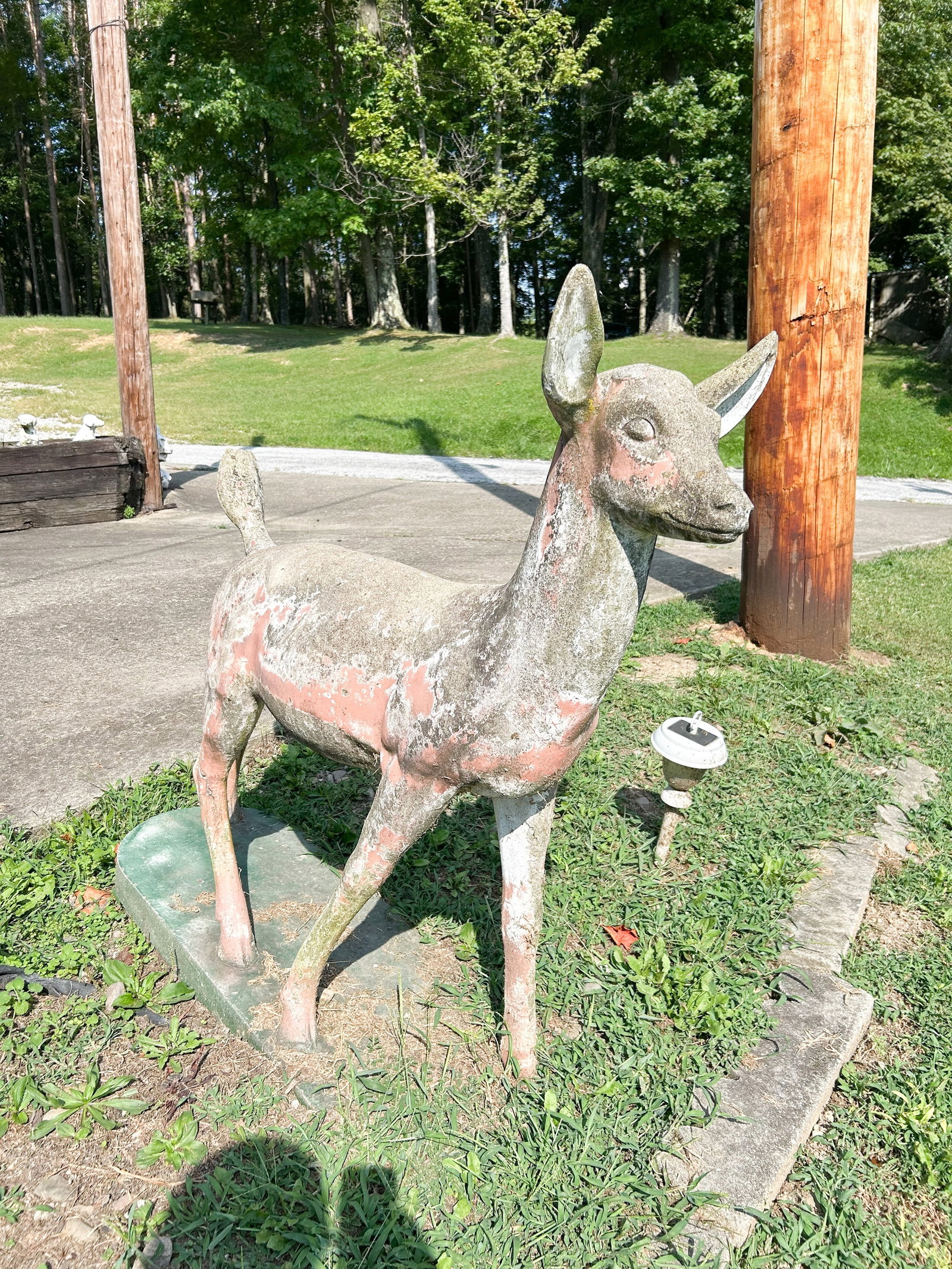 CAST STONE FAWN GARDEN STATUE, MID-20TH CENTURY: A mid-century cast stone garden sculpture depicting a standing fawn on an integral rectangular base. The figure features a naturalistic form with upright ears and remnants of a polychrome painted fini